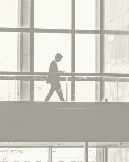 A lone figure crossing a skywalk in a glass-walled building